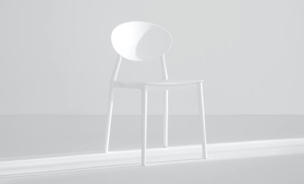 A very white ambient with a chair on the center receiving sun light.